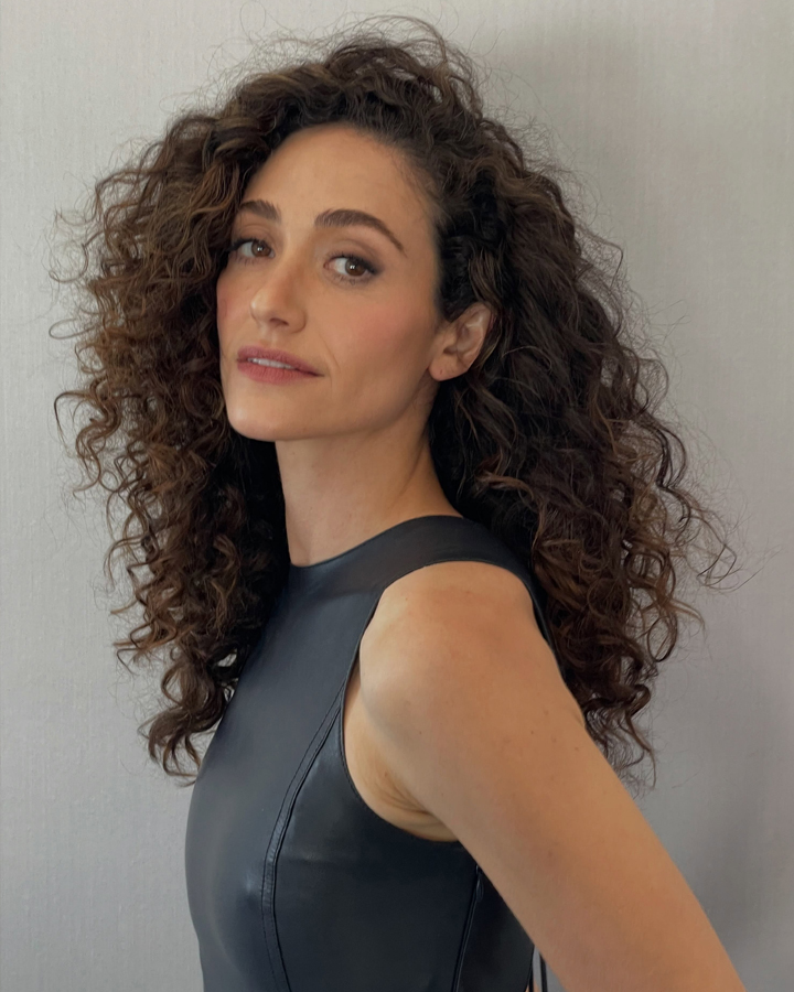 Portrait of Emmy Rossum from the chest up looking at the camera on a gray background